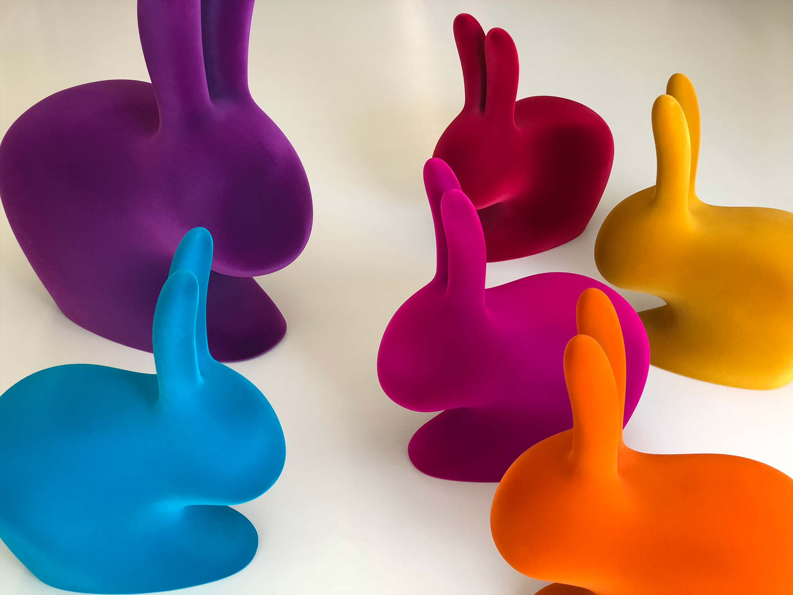 Close up of multicolored rabbit chairs arranged on a white surface with purple pink blue and orange tones