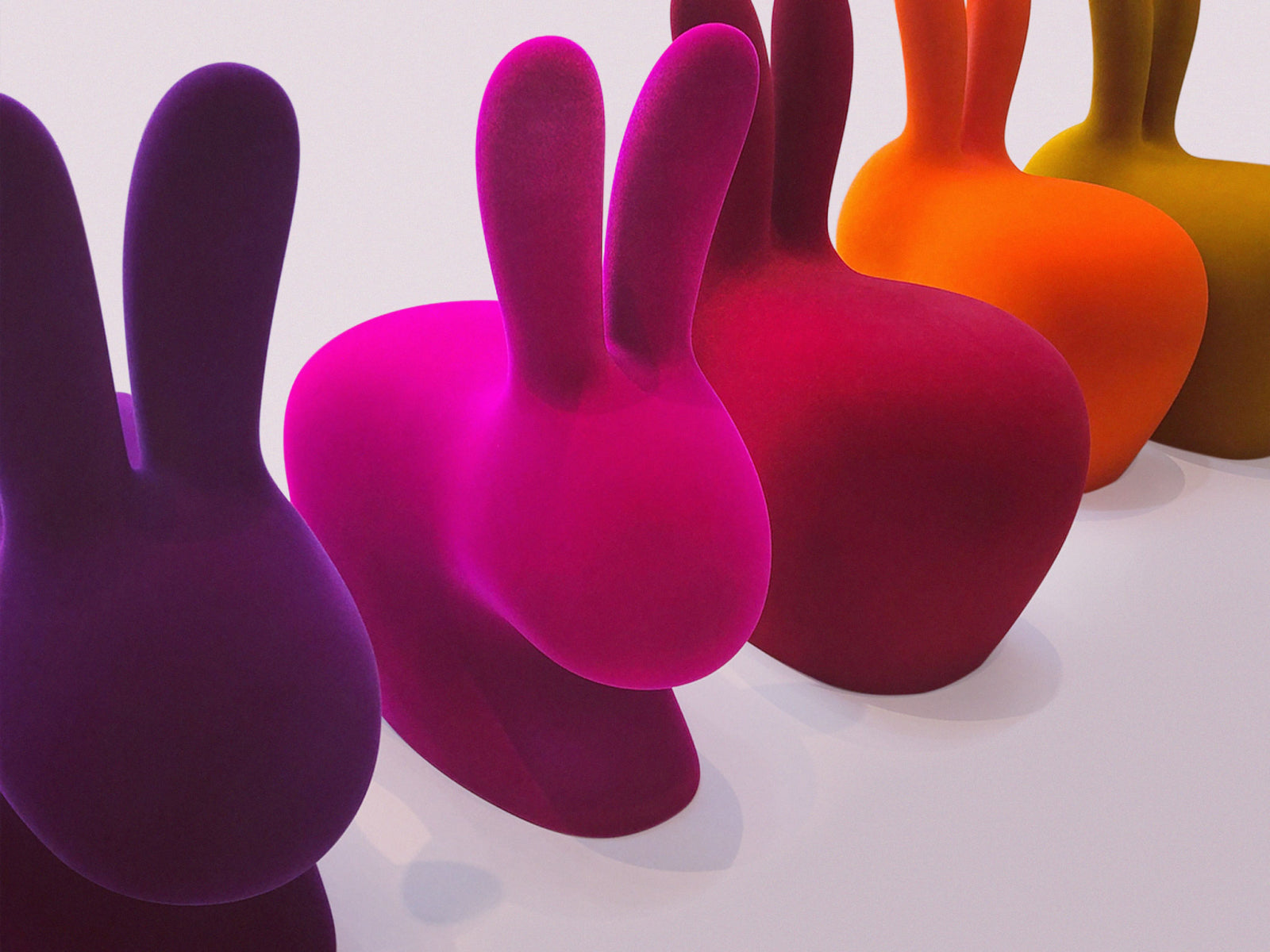 Row of Rabbit Chairs in vibrant velvet colors arranged in a line on a white surface