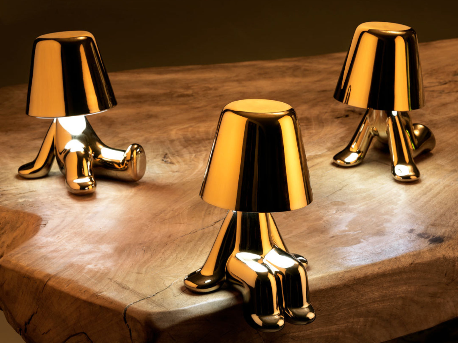 Three Tom lamps from the Golden Brothers on a warm wooden table, their gleaming gold forms catching the light.