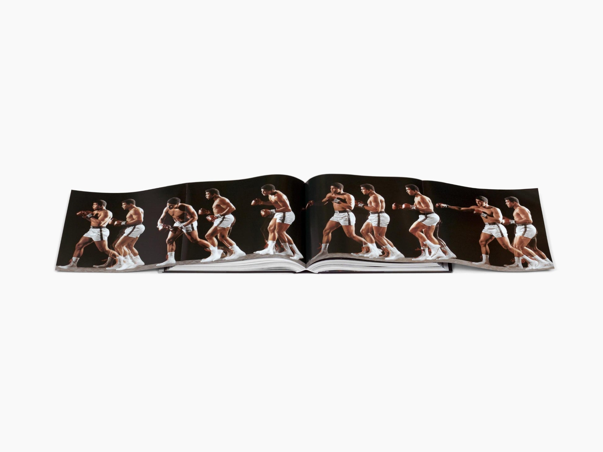 Open book showing a continuous sequence of Muhammad Ali boxing poses in white trunks across two pages.