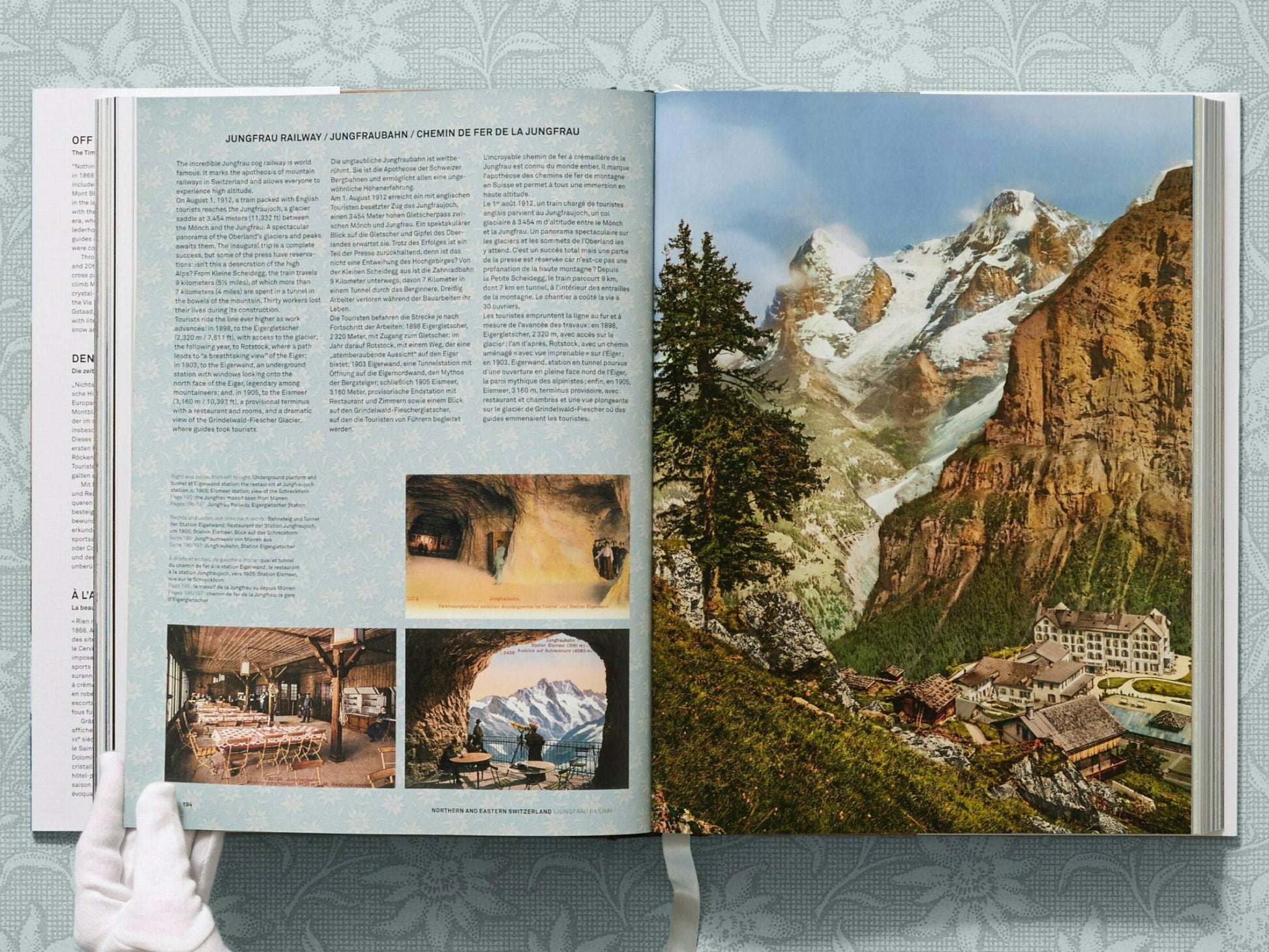 Open book spread showing a panoramic alpine valley with snowcapped peaks and a village at the base.