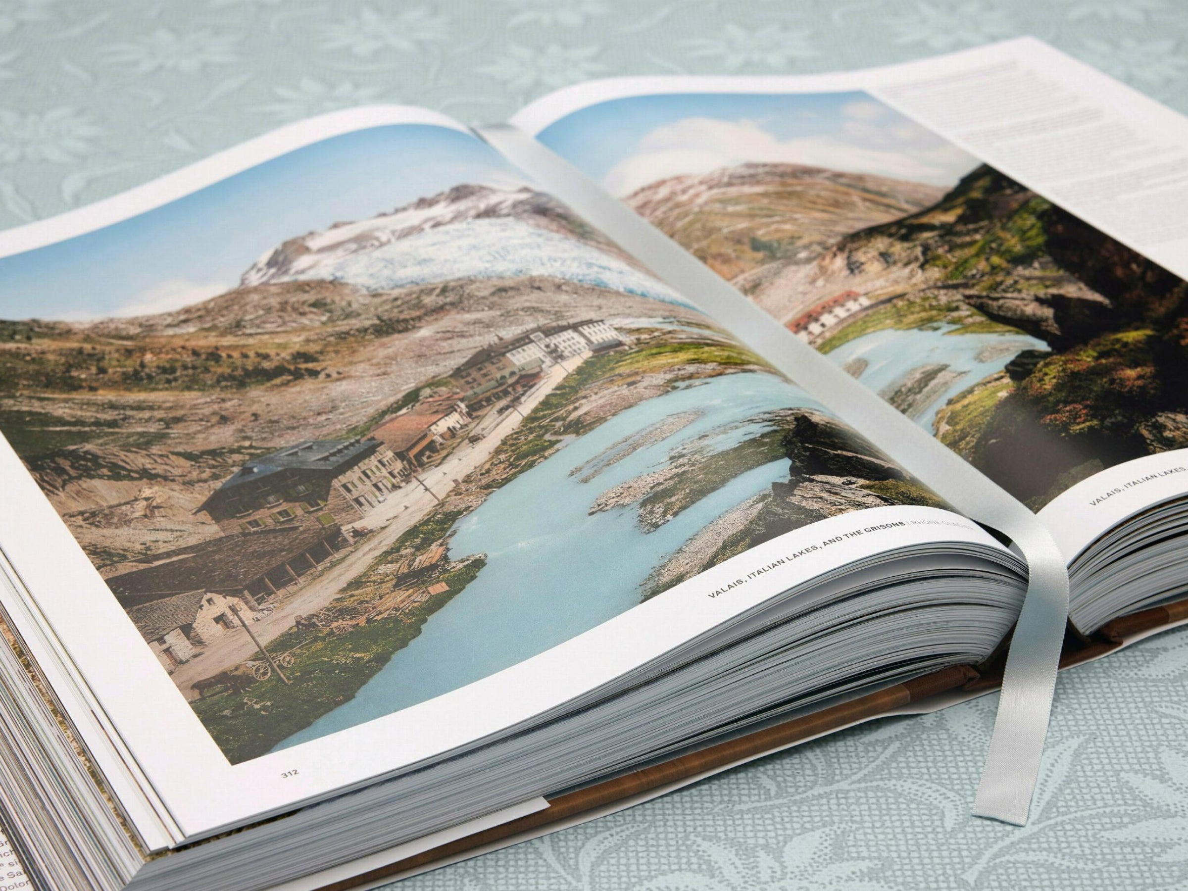 Interior page spread depicting a mountain town along a turquoise lake with soaring alpine peaks.