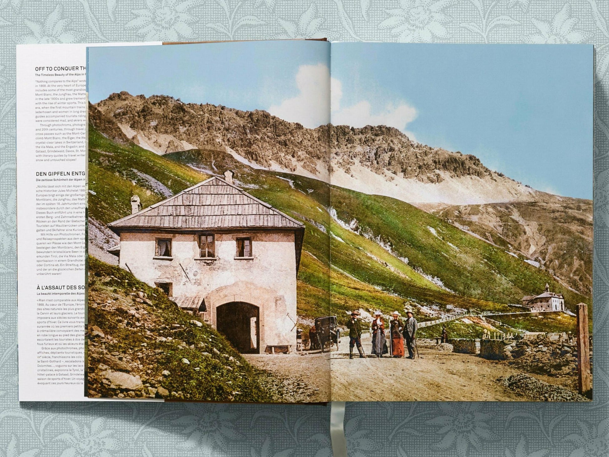 Stone building on a hillside with a winding path and green slopes leading to distant snow covered peaks
