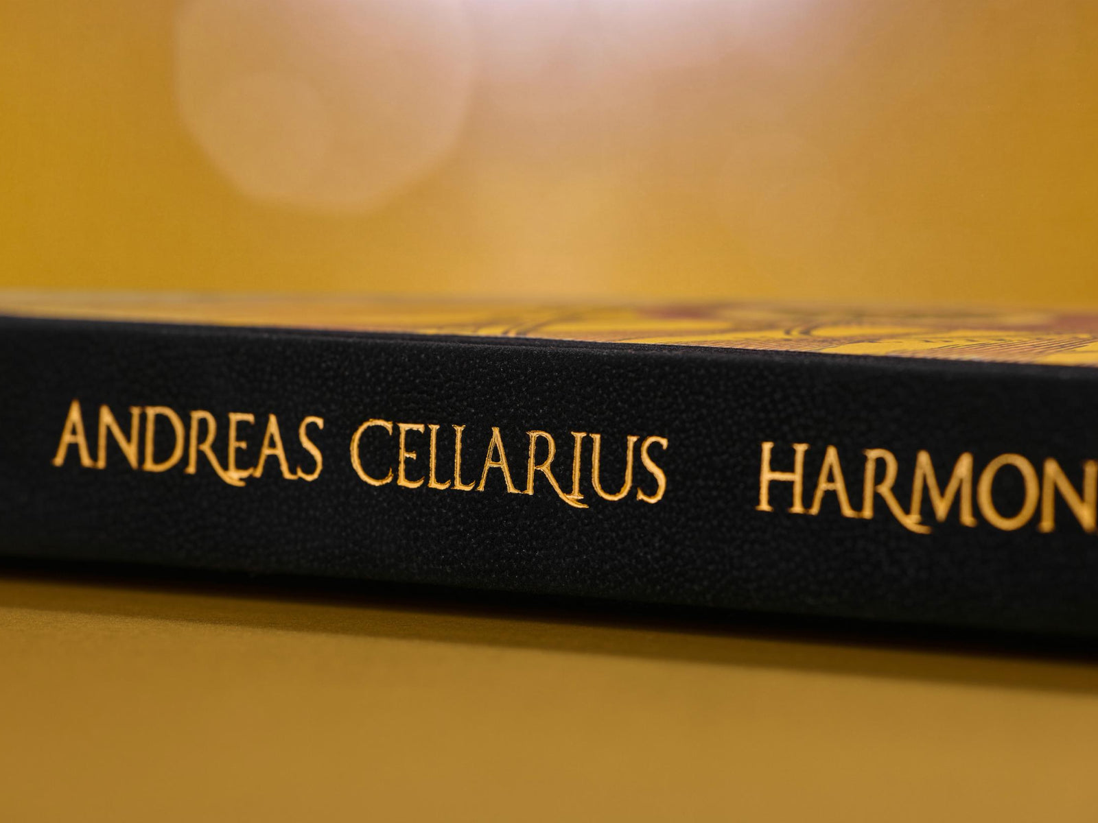 Spine view of the Cellarius Atlas with gold lettering Andreas Cellarius Harmonia Macrocosmica on a black binding beside map imagery.