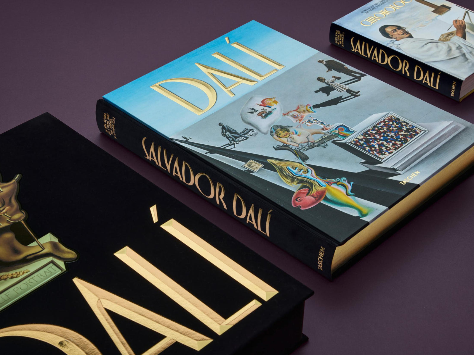 Two Dalí books on a purple surface, a large blue DALI volume and a smaller portrait edition nearby.