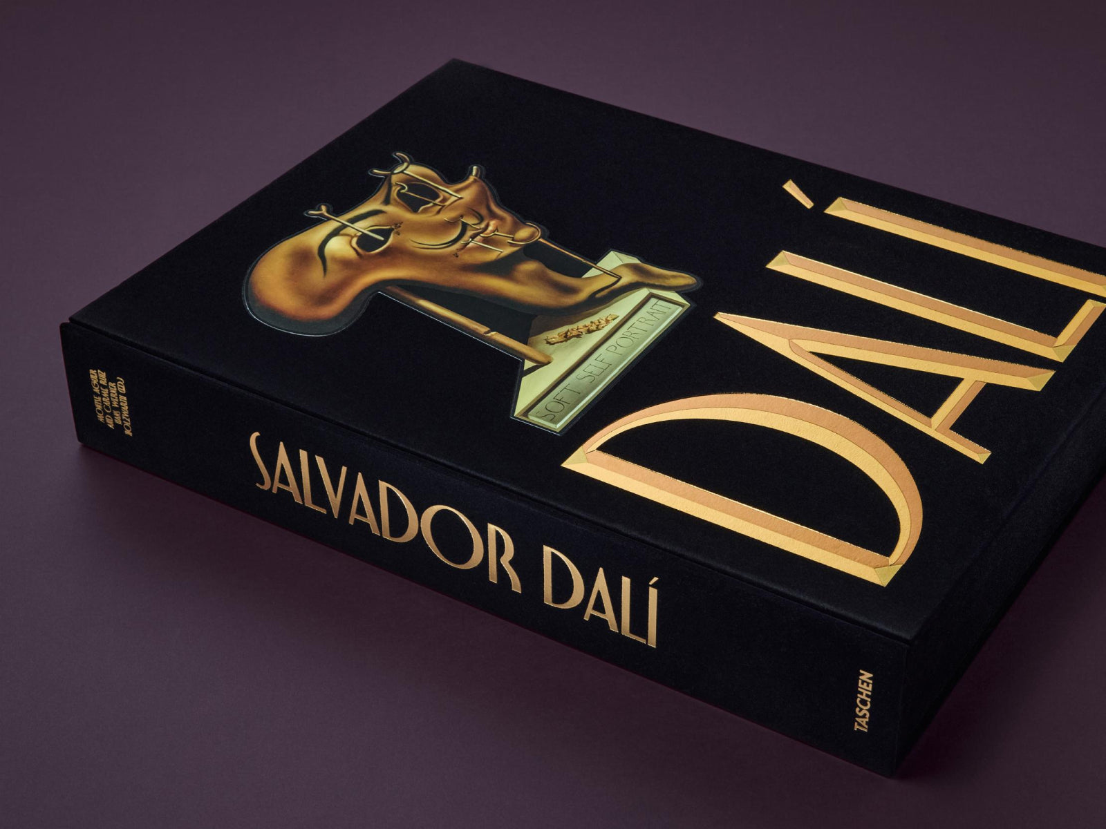 Side view of Dalí Chronology book showing black spine with gold vertical title against a purple backdrop