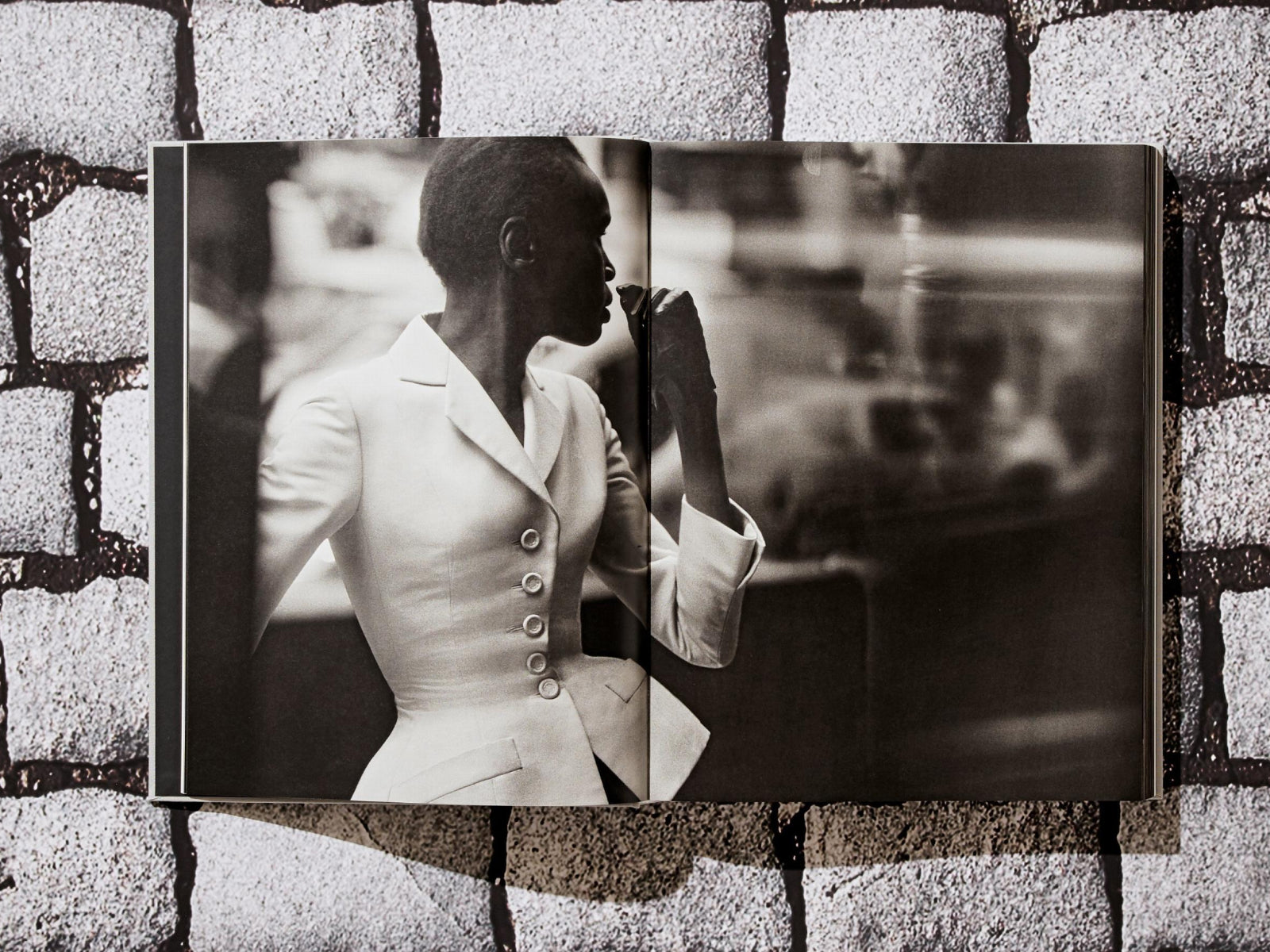 Black-and-white page from Peter Lindbergh Dior featuring a model in a white tailored suit posed against an urban backdrop.