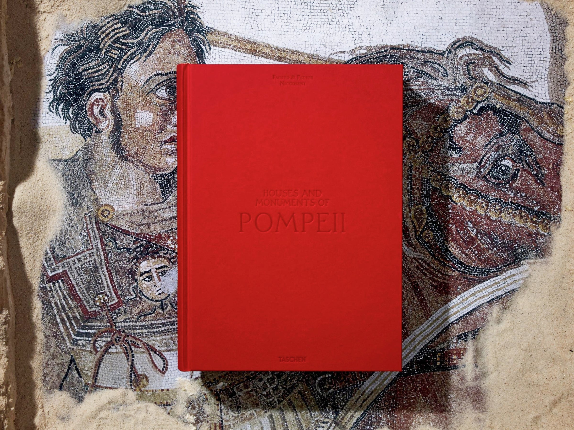 Red Pompeii book resting on a mosaic floor with a dark cover and gold detailing.