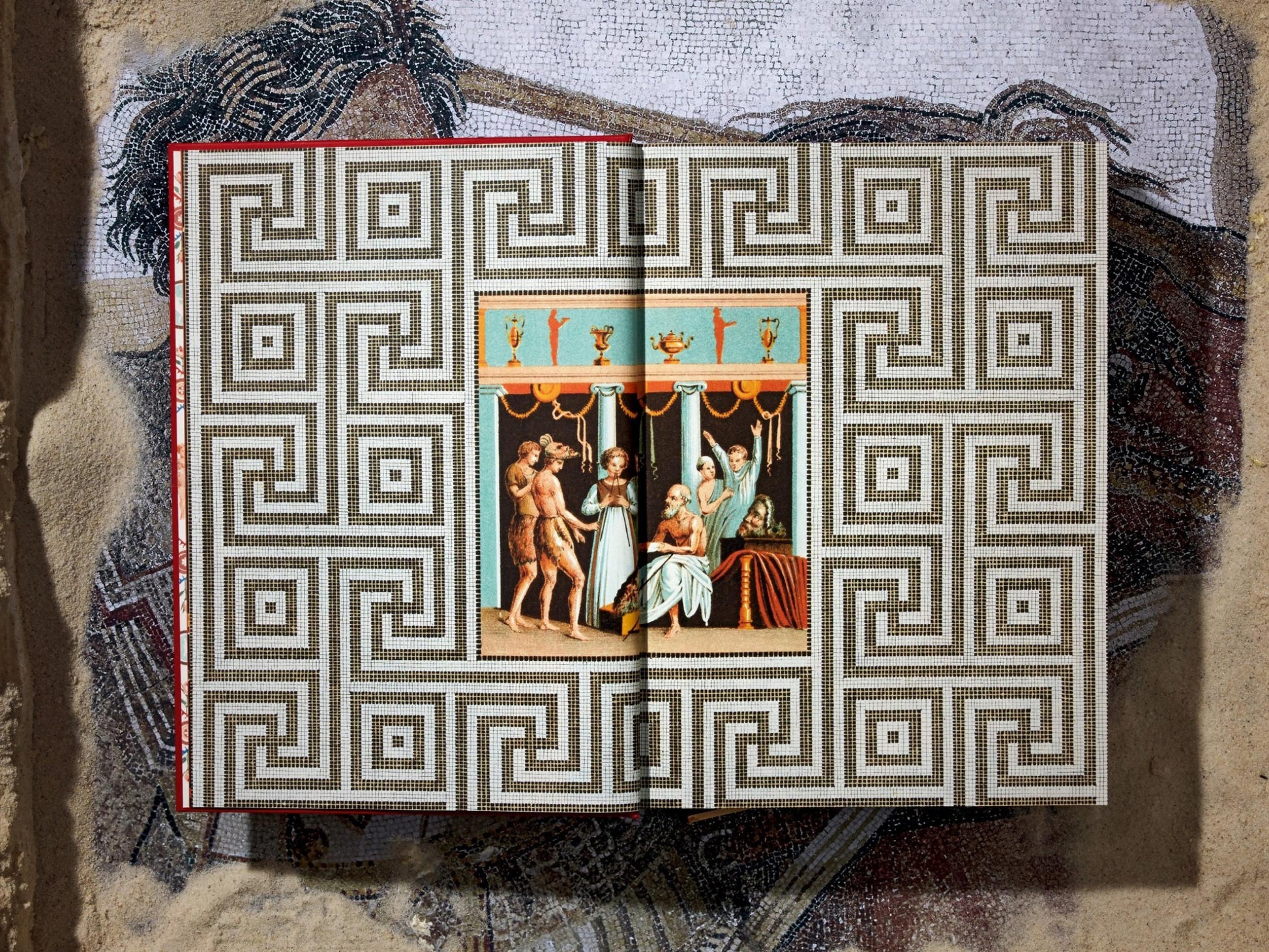 Open book with a black and white geometric labyrinth pattern and a small central color painting.