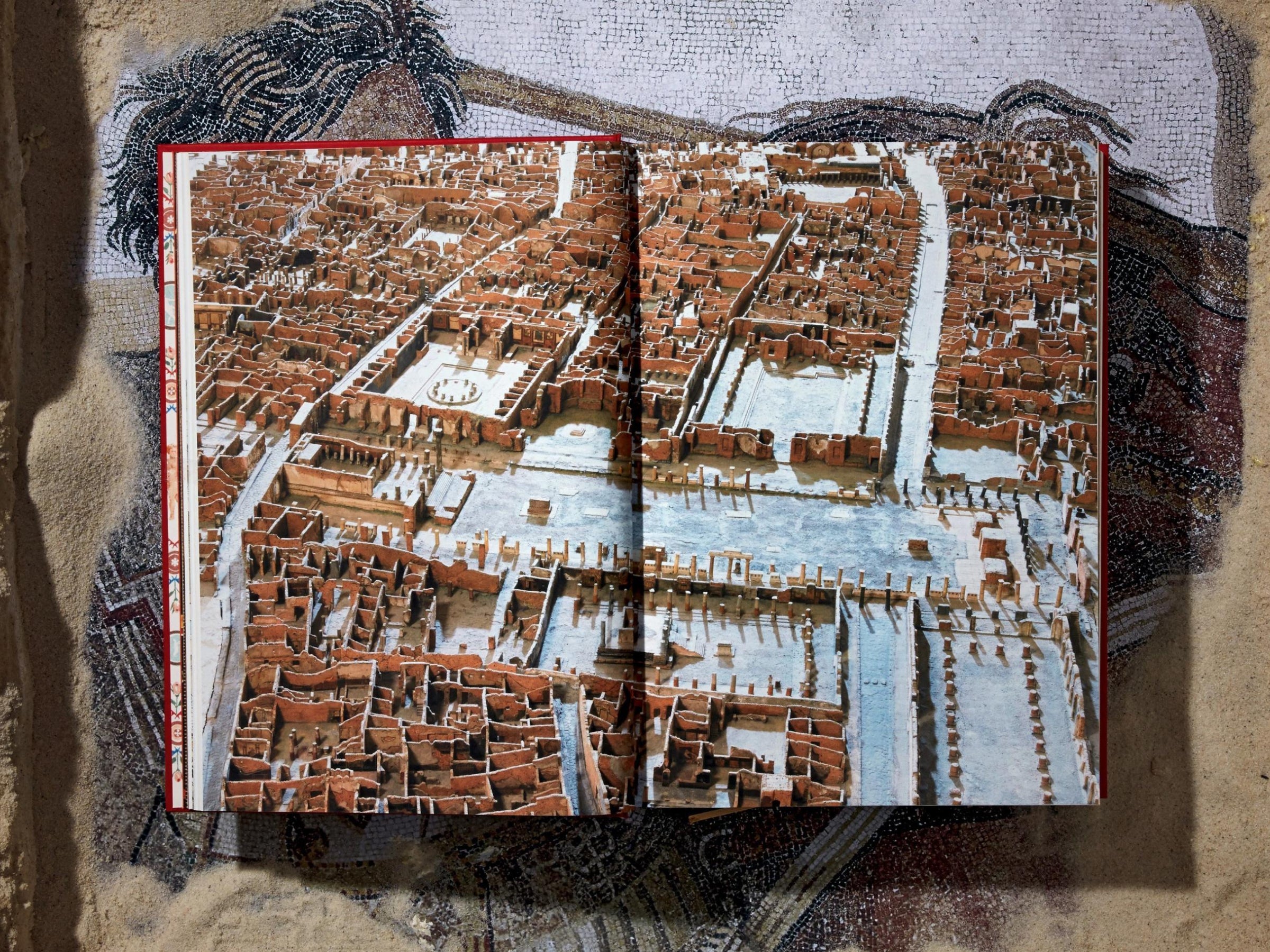 Open book spread showing an aerial view of Pompeii ruins with brick walls and narrow, intersecting streets.