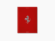 Red hardcover Ferrari book standing upright with a silver prancing horse emblem on the cover.