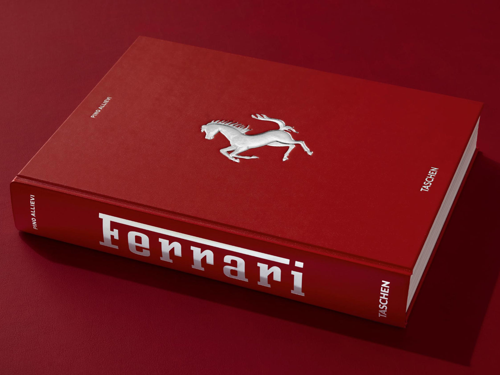 Red hardcover Ferrari book with silver prancing horse logo on a red surface.