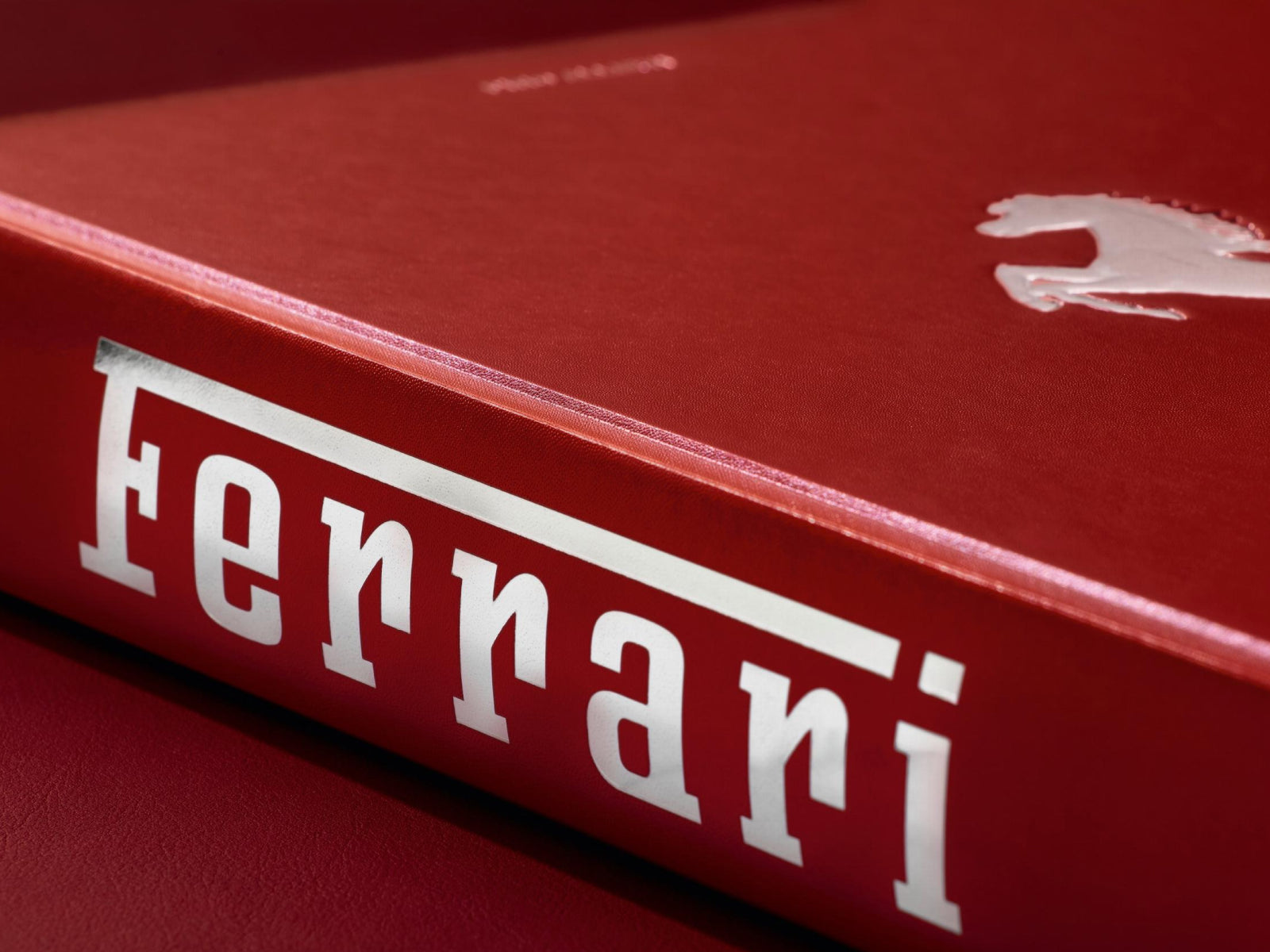 Open red Ferrari book spread showing large white Ferrari typography across both pages.