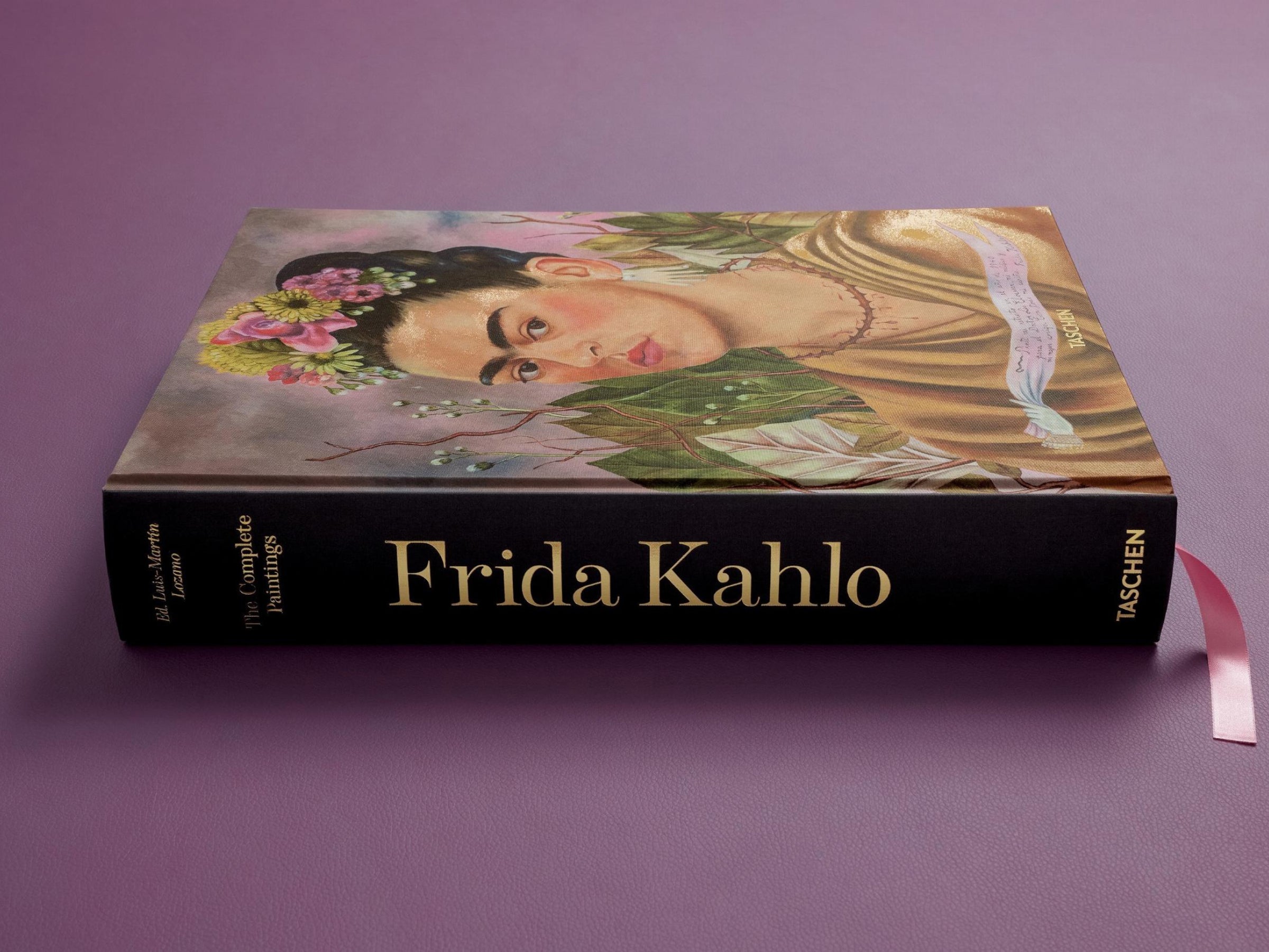 Frida Kahlo complete paintings book lying on its side on a purple surface with a pink ribbon.
