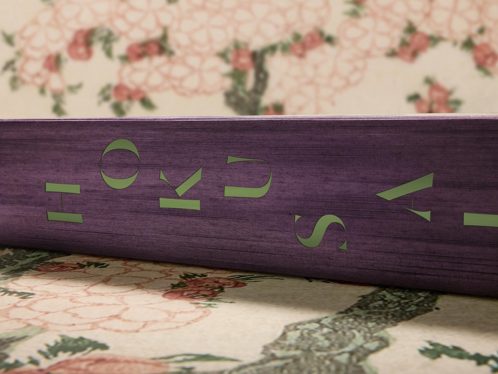 Purple cloth bound Hokusai volume with green lettering resting on a floral backdrop.