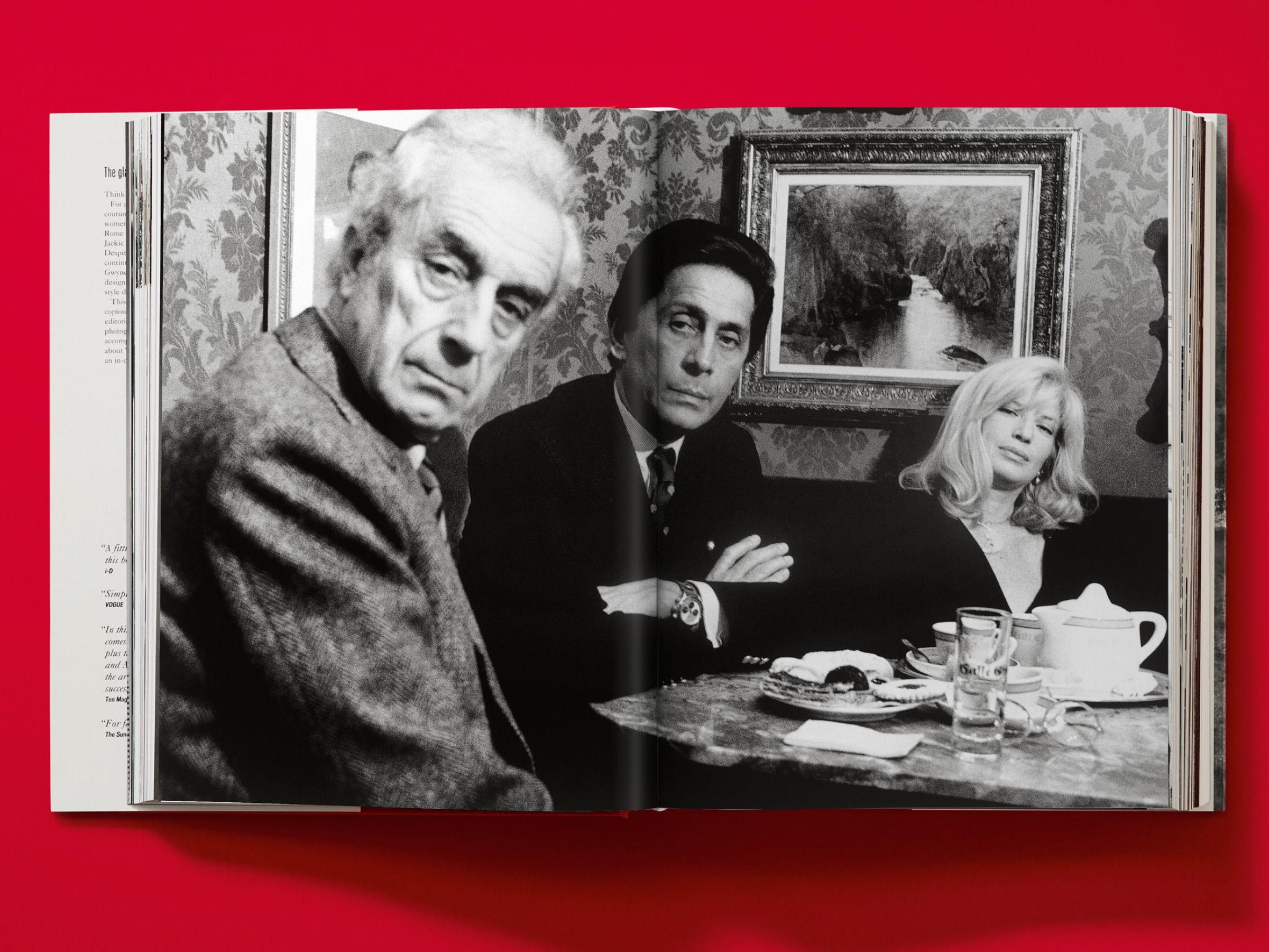 Open book spread showing a black and white photo of three people at a table in a richly decorated room.