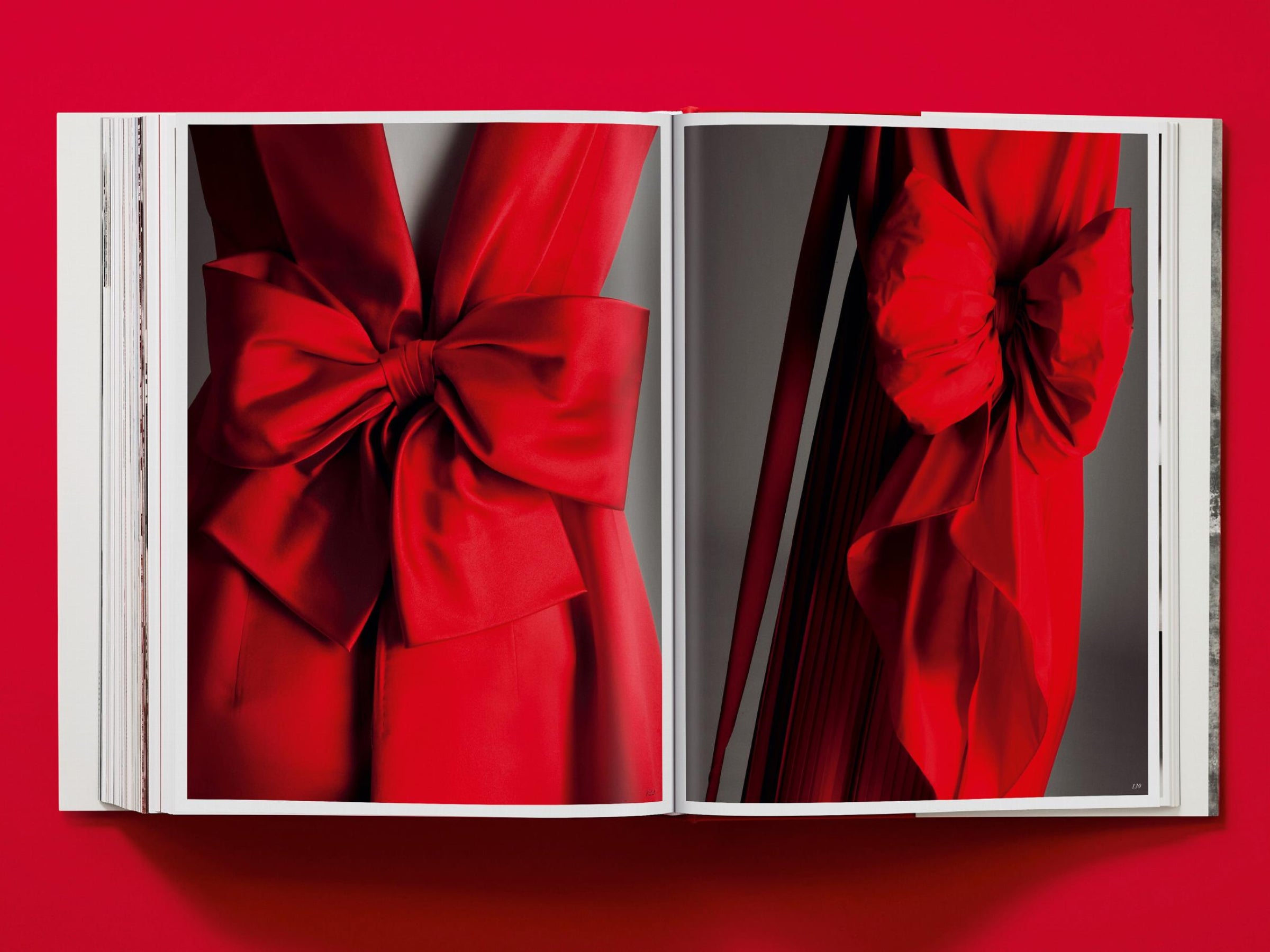 Open book spread from Valentino couture volume showing a dramatic red satin bow across the two pages.