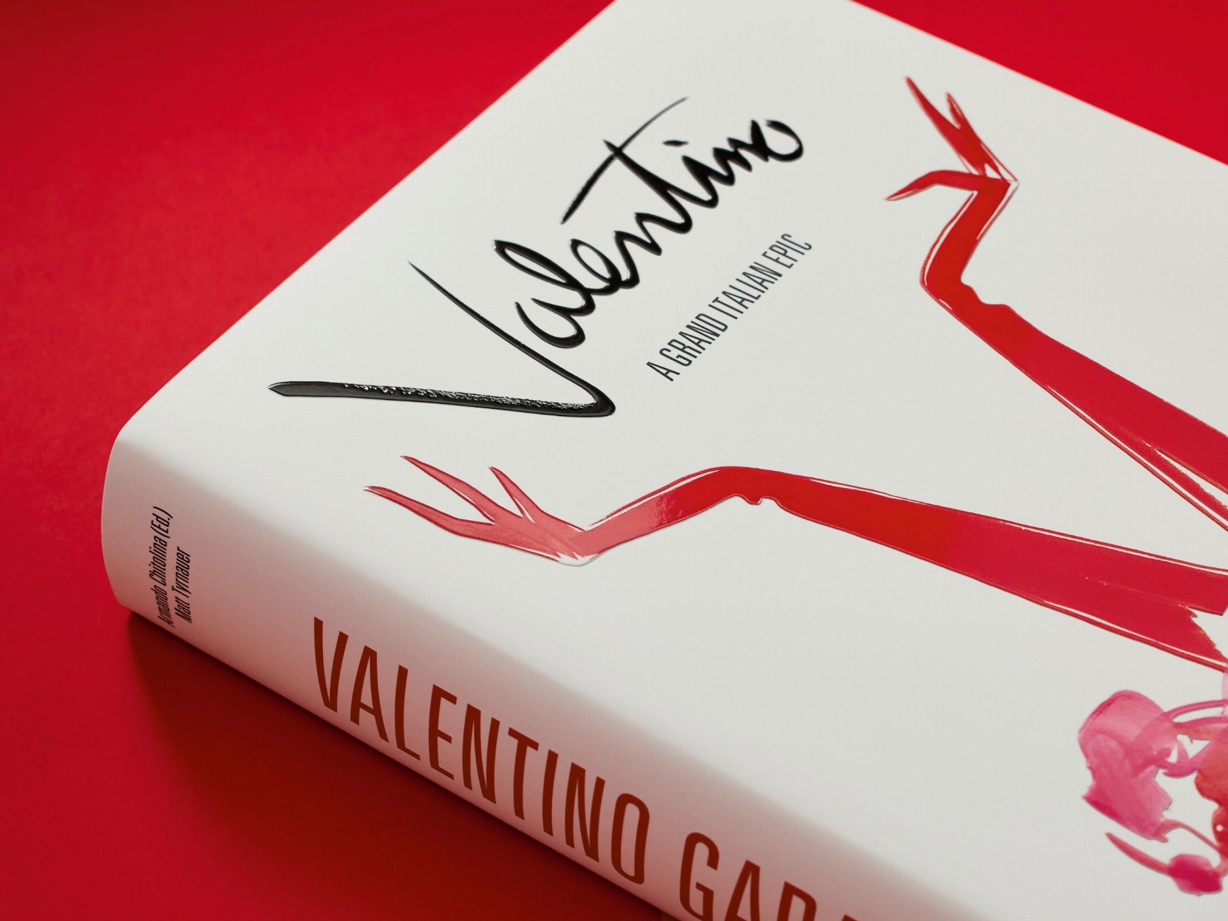 Close-up tilted view of Valentino A Grand Italian Epic cover against a red backdrop featuring the red arm graphic.