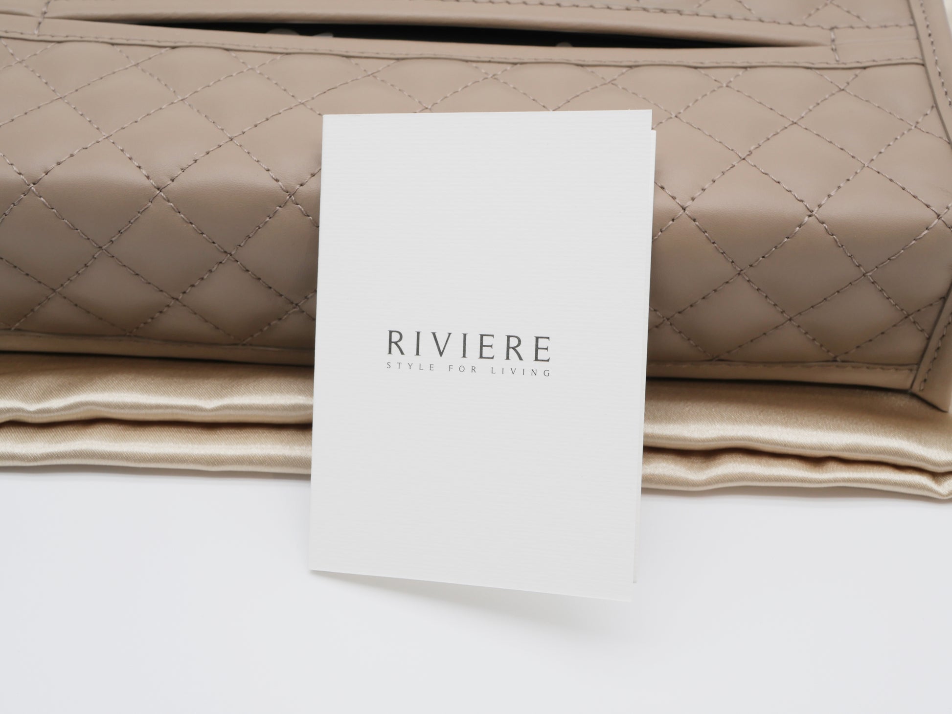 Beige quilted tissue holder with chrome trim and a branding card in front