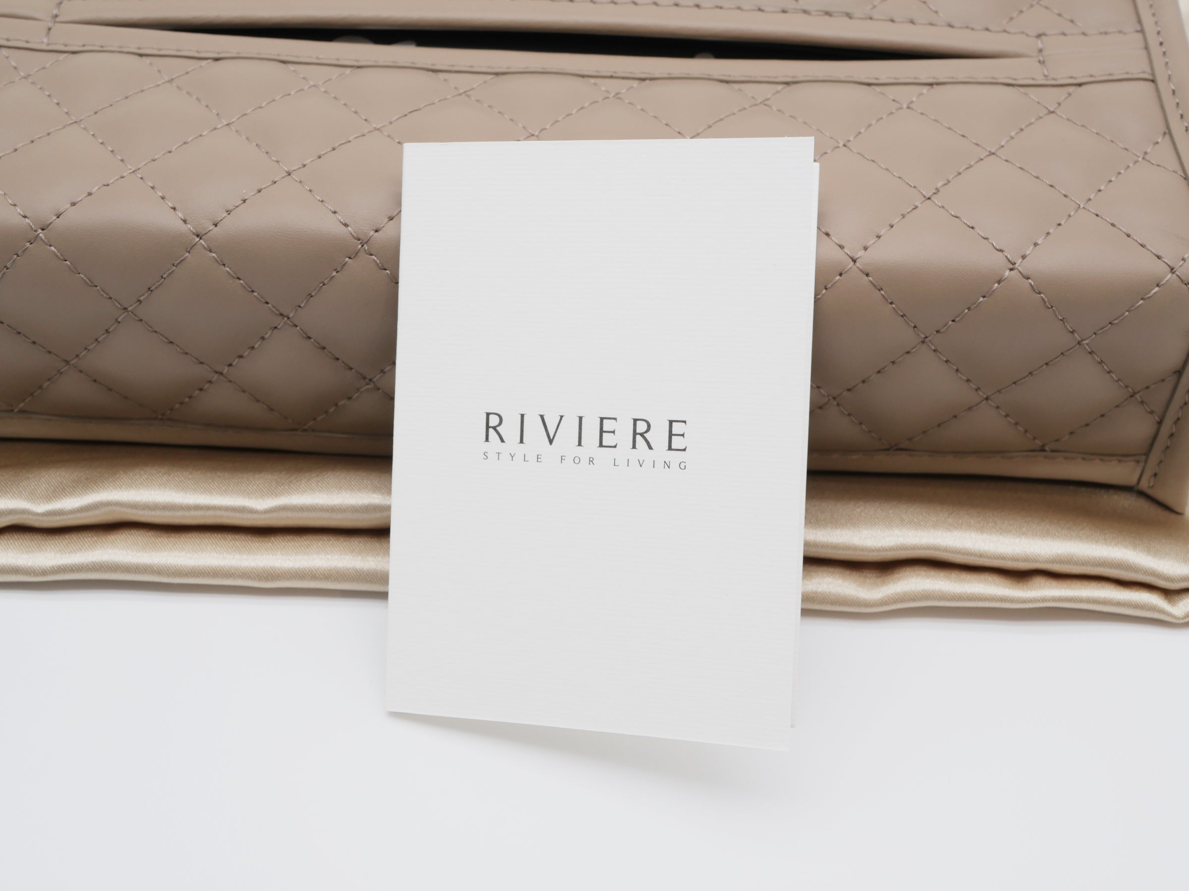 Beige quilted tissue holder with chrome trim and a branding card in front