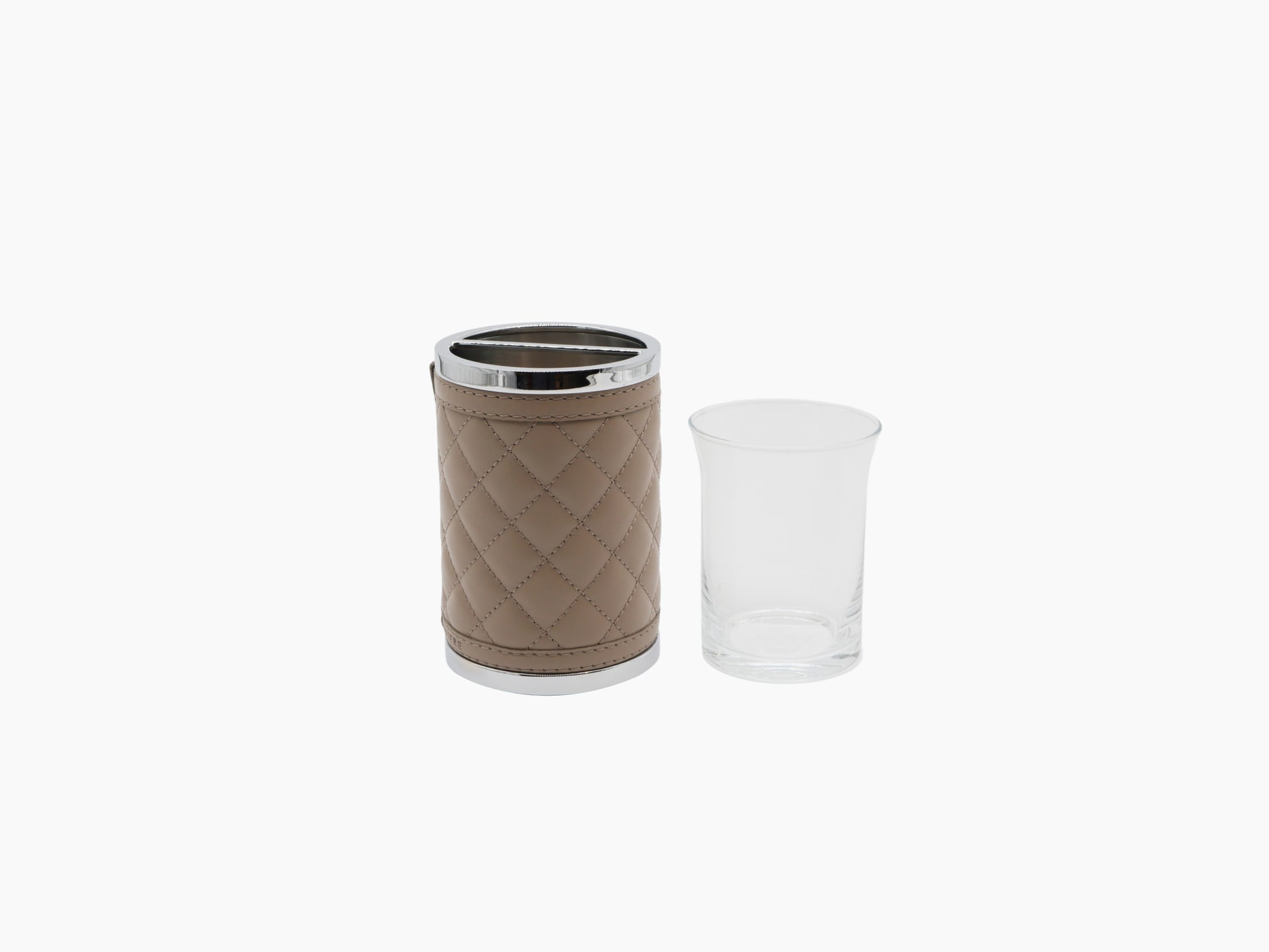 Beige quilted leather toothbrush holder with chrome top beside a clear glass tumbler
