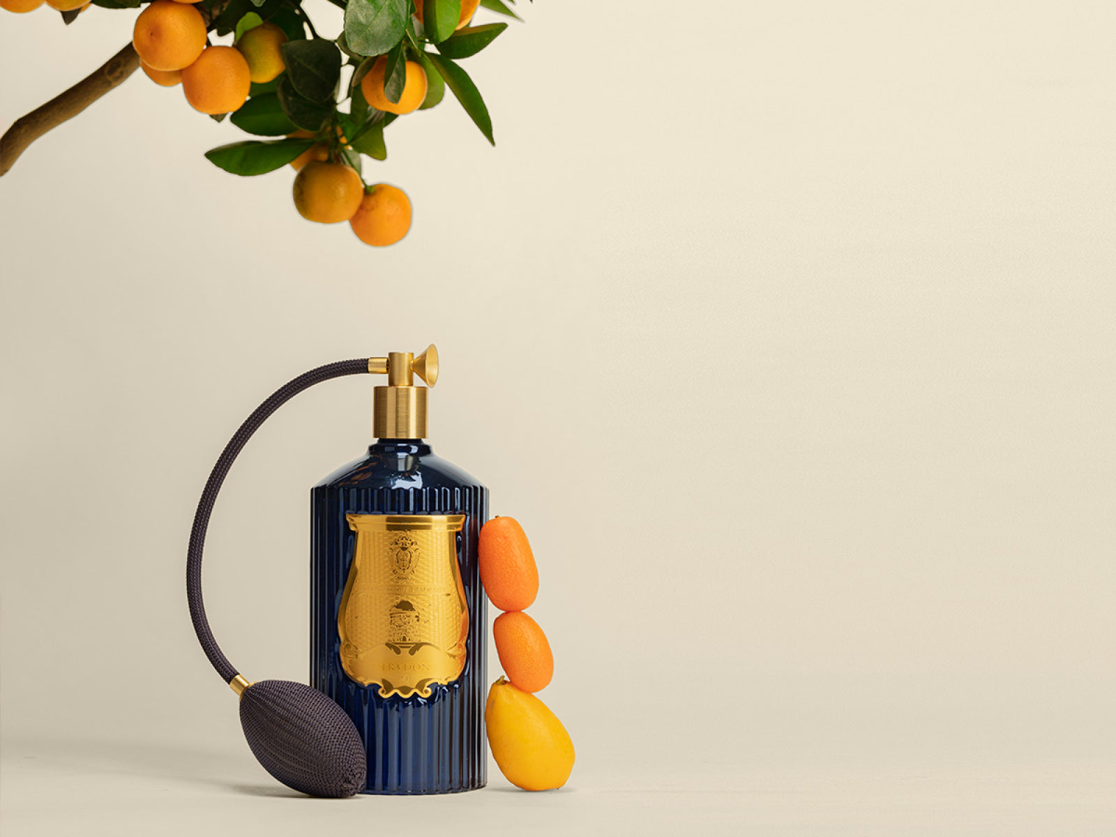 Reggio room spray in fluted deep-blue bottle with gold label beside a branch of ripe oranges.