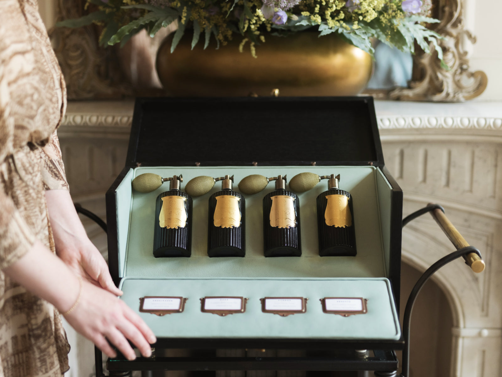 Four deep blue room spray bottles with gold labels and woven pumps in an open pale blue case.