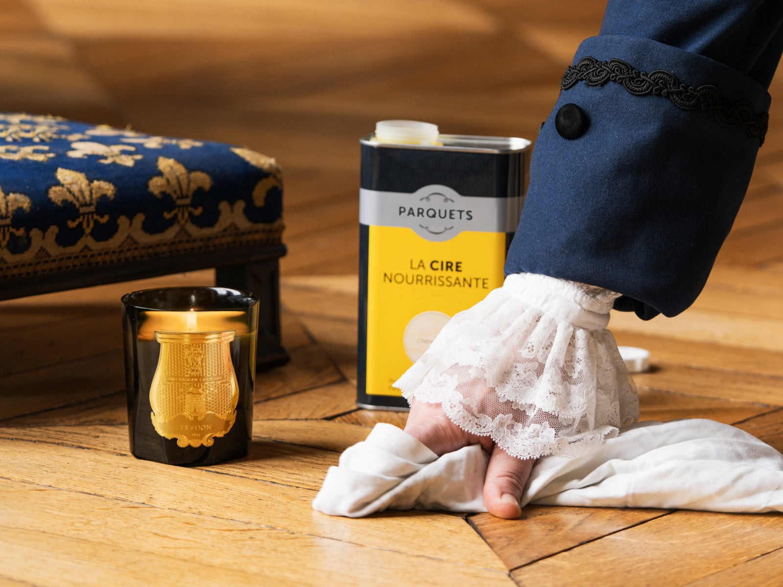 Joséphine Floral Garden scented candle in a black glass with a gold crest on a wooden floor beside a yellow La Cire Nourrissante can