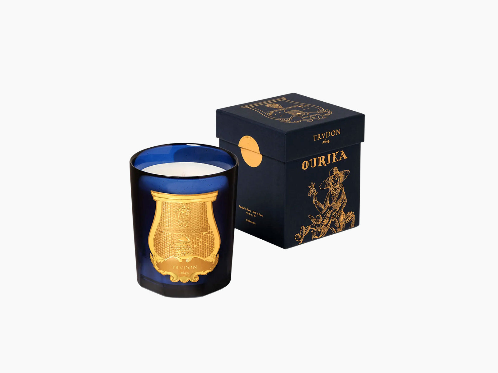 Blue glass candle holder with a gold ornate plaque beside a dark navy Ourika box with gold artwork