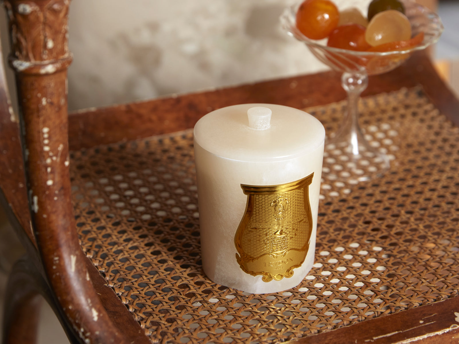 White alabaster candle container from Gabriel with gold emblem resting on a woven table.