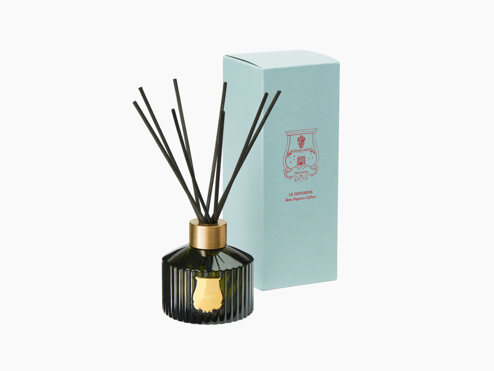 Gabriel diffuser in dark green ribbed glass with a gold emblem and black reeds beside a pale turquoise box