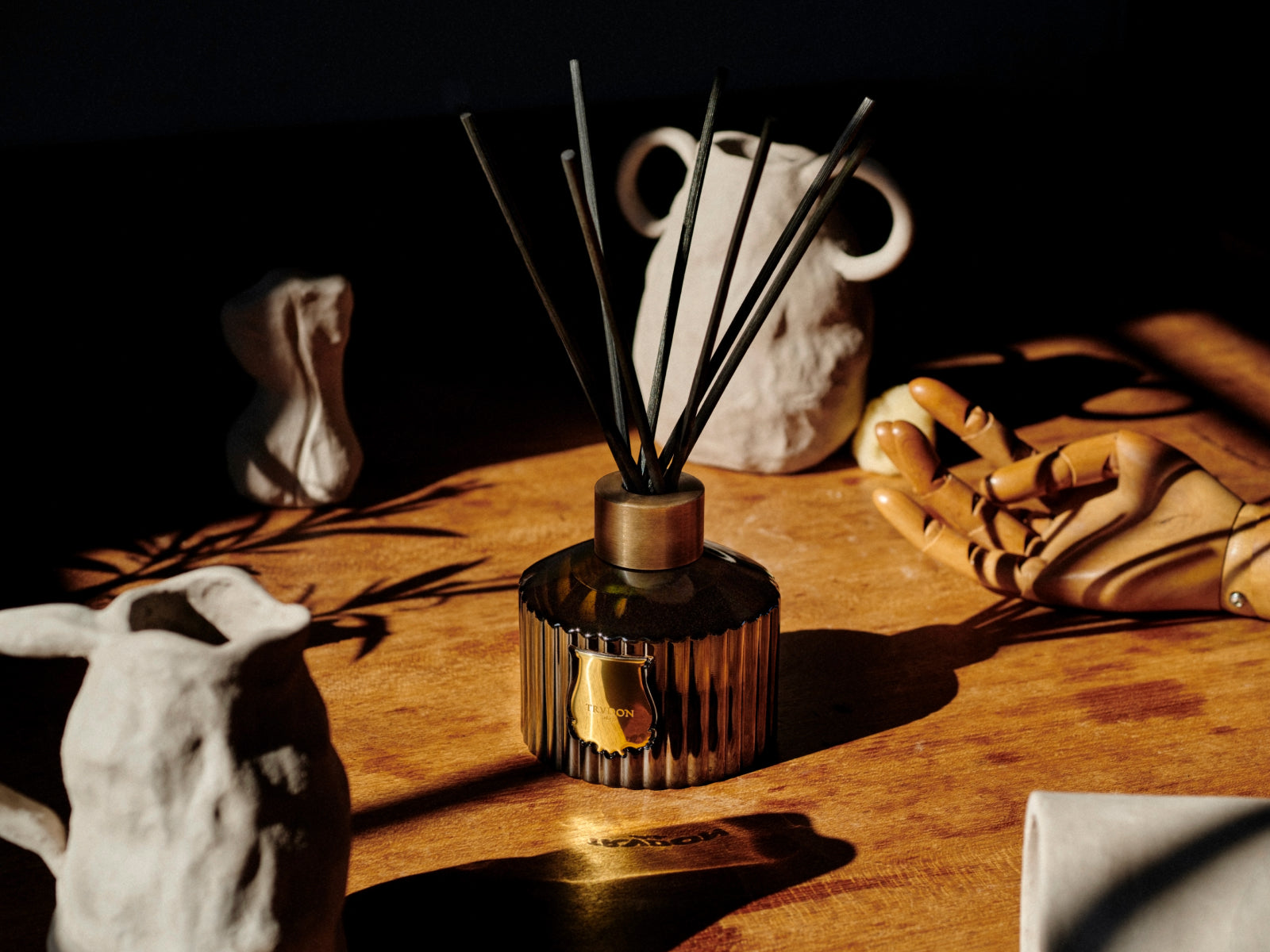 Two Gabriel diffusers in green glass with gold collars and black reeds on a marble surface.