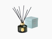 Dark green ribbed diffuser bottle with black reeds and a gold neck beside a pale blue box.