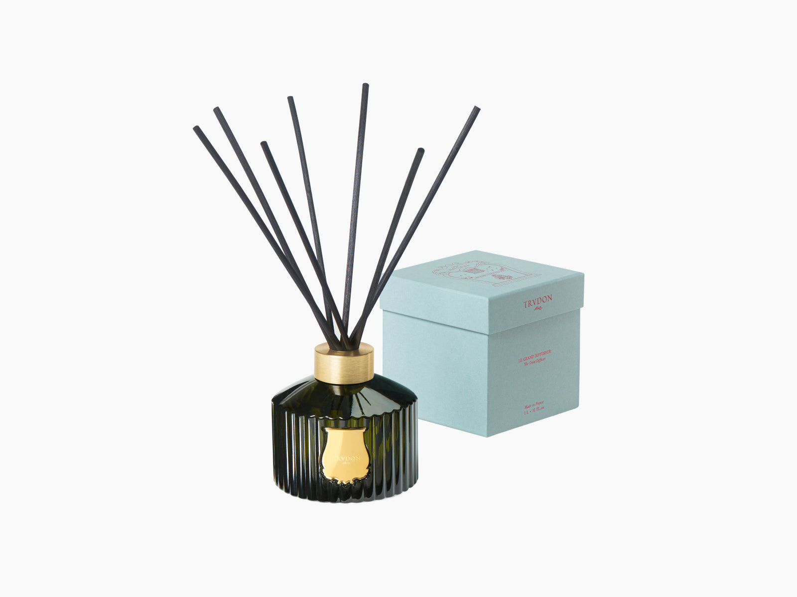 Dark green ribbed diffuser bottle with black reeds and a gold neck beside a pale blue box.