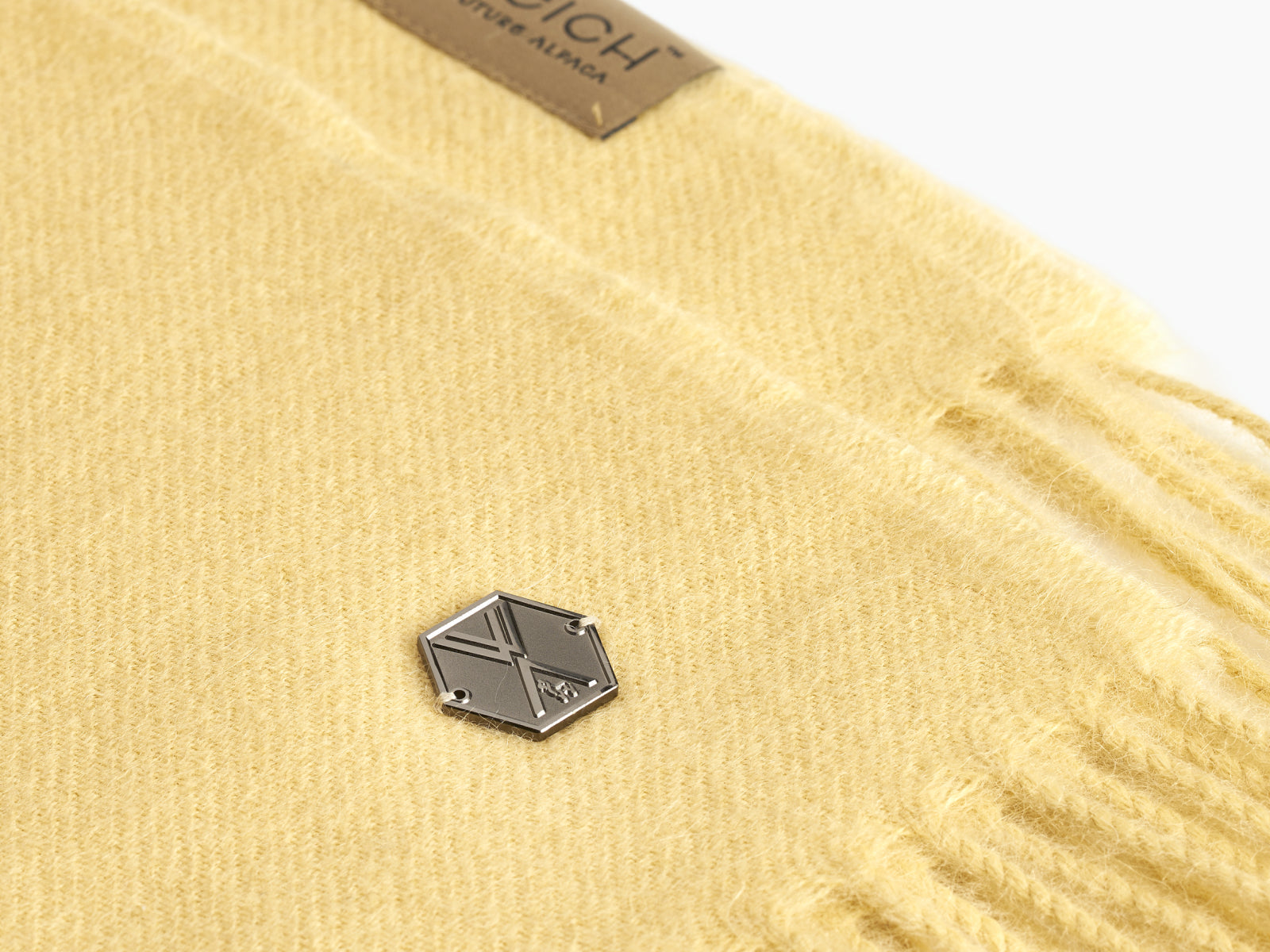 Plaid ALMA alpaca blanket in beige with a small metal hex tag on soft knit fabric