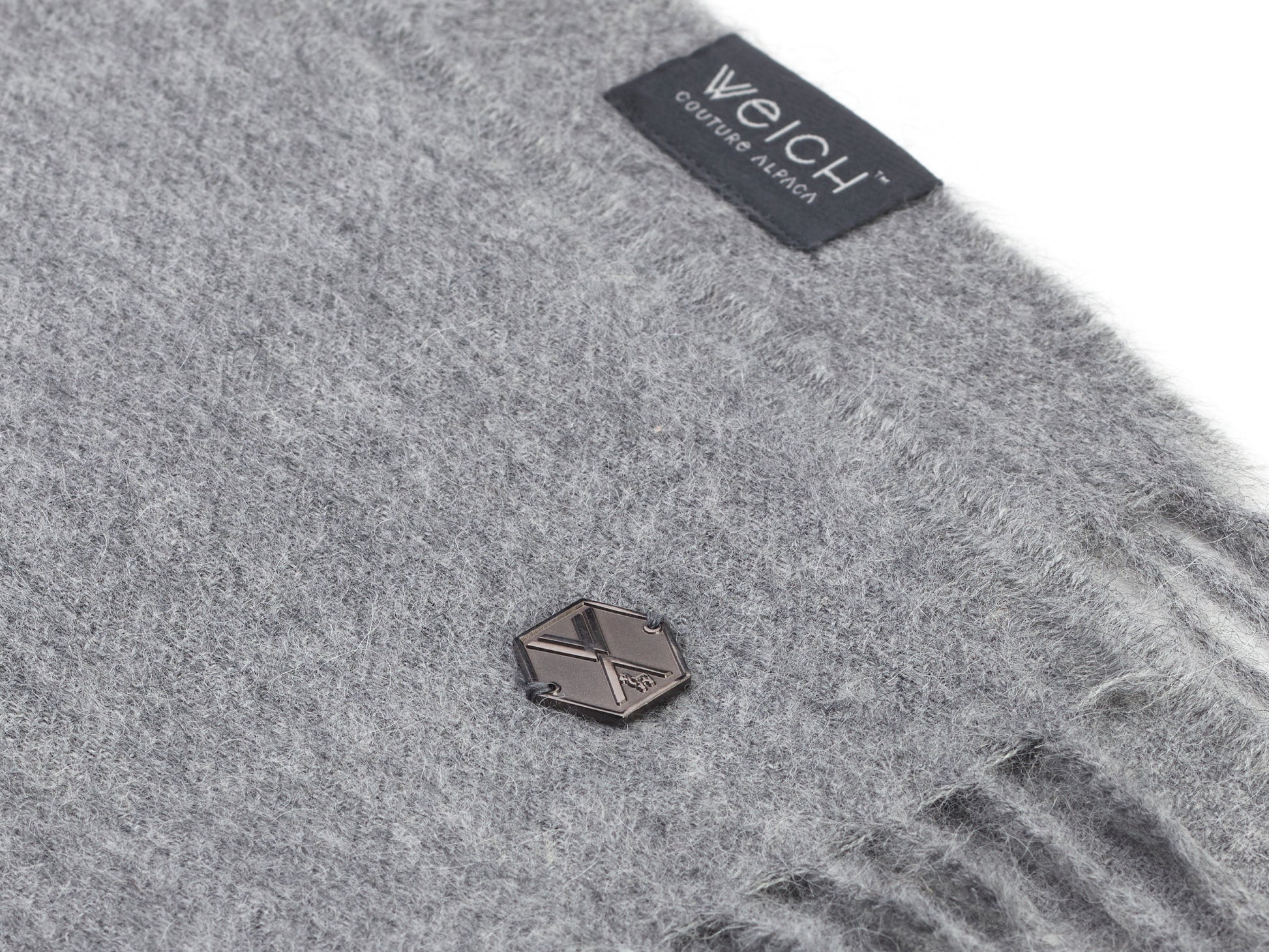 Grey alpaca Plaid ALMA blanket close up with soft fuzzy texture and metal emblem tag.