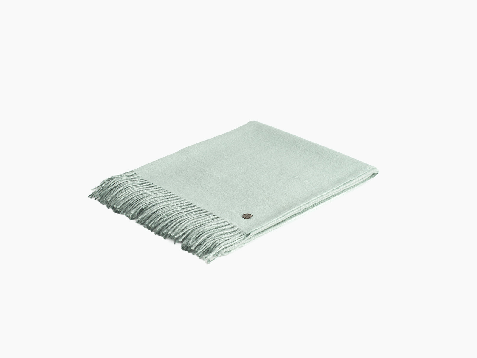 Angled view of mint green Plaid ALMA alpaca blanket showing fringed edge