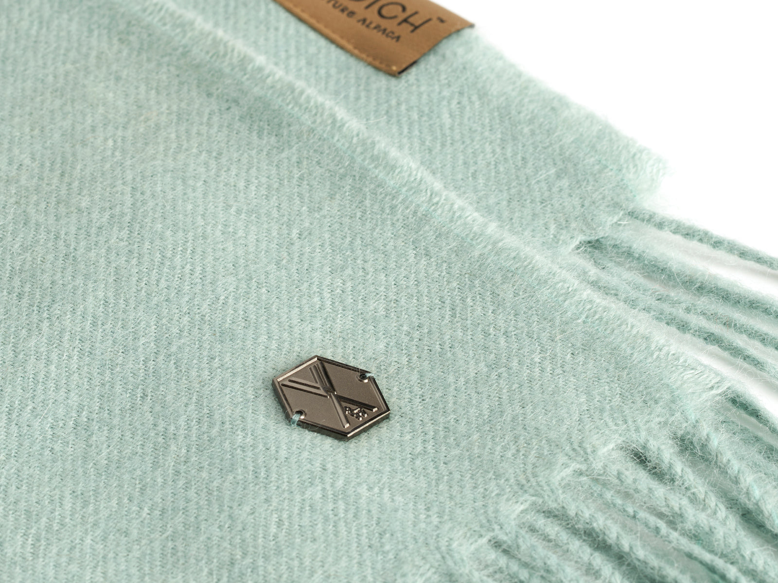 Close up of mint green Plaid ALMA alpaca blanket fabric with a small metal tag