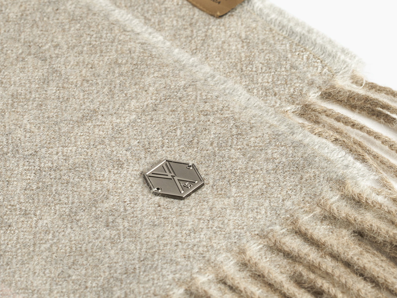 Close-up of a beige BORREA alpaca blanket with fringe and a metal tag.