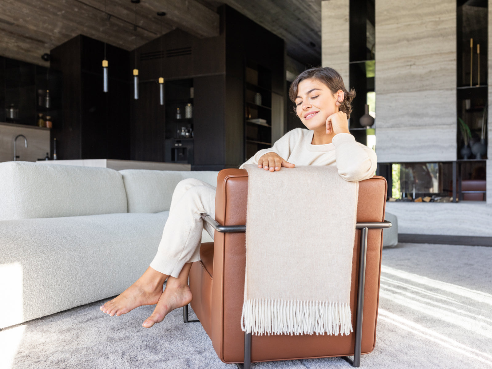 Woman relaxing on a brown leather chair with a beige throw draped over the back in a modern living room
