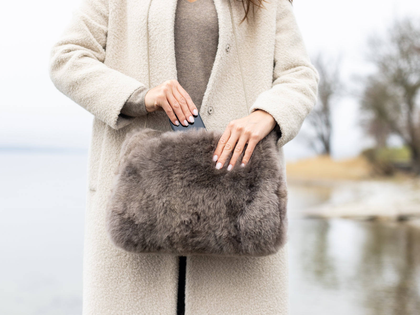 Person in a beige coat holds a taupe fur pocket muff outdoors
