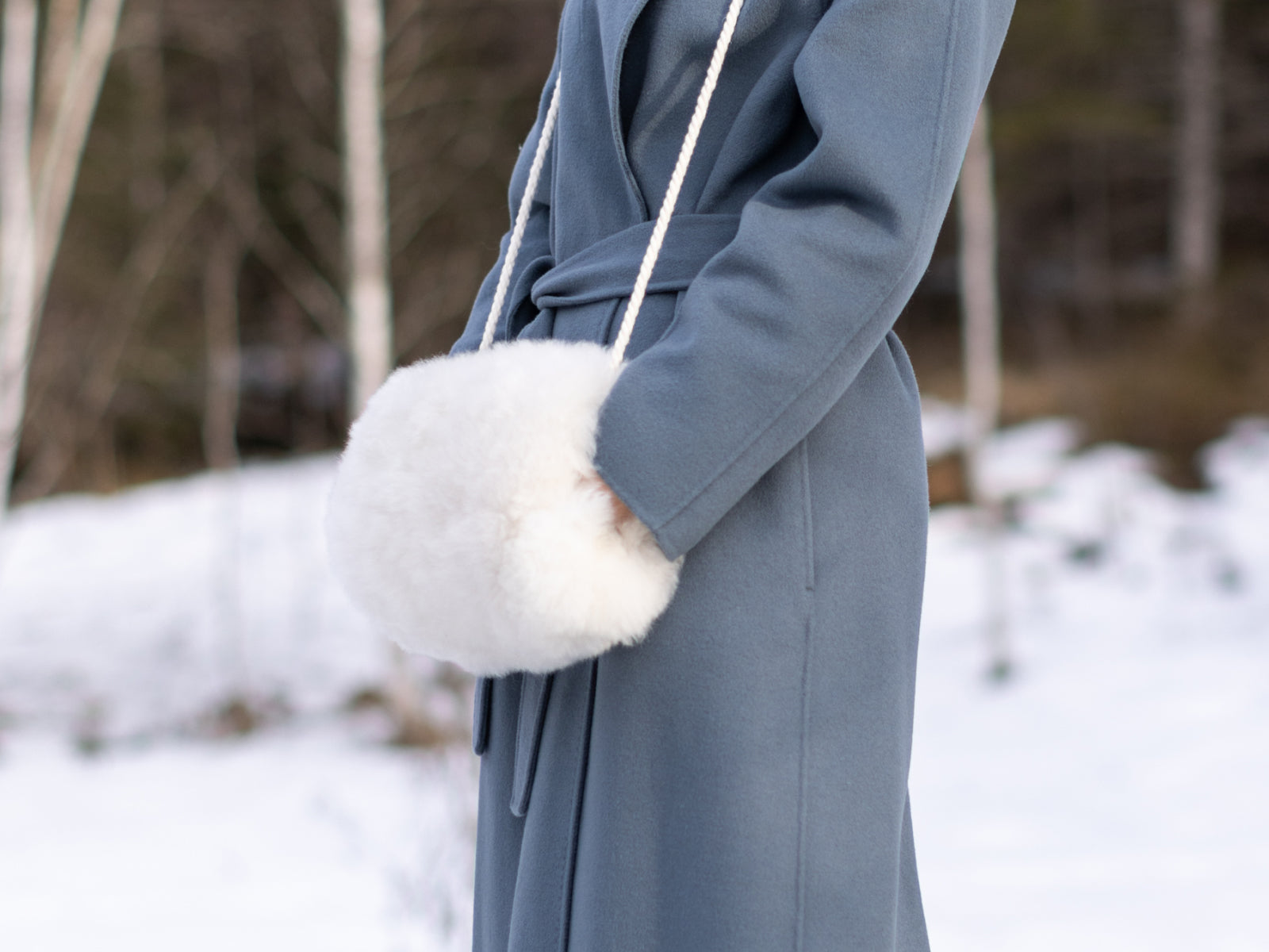 Close-up of a fluffy white alpaca pocket muff with a rope strap against a blue coat.