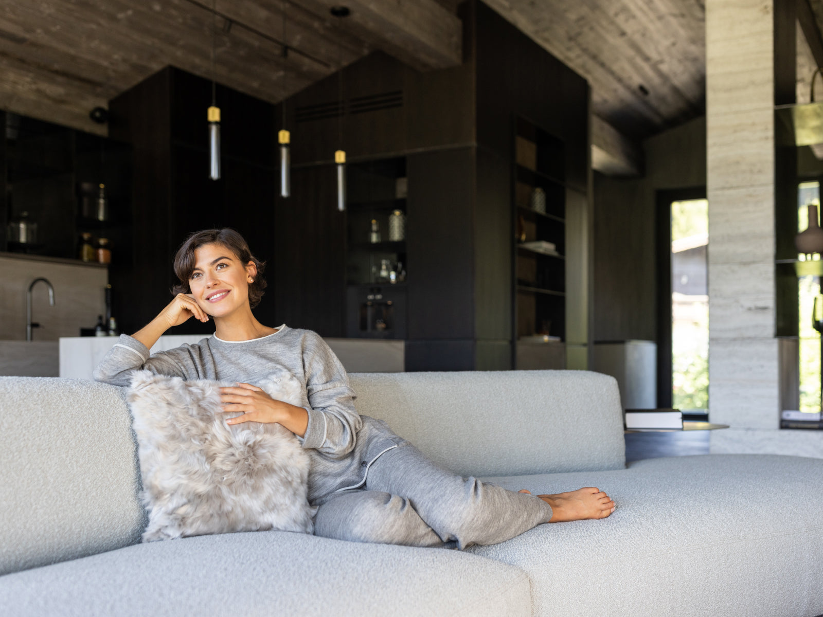 Woman relaxing on a pale gray sofa with a soft alpaca fibre cushion in a modern living room.