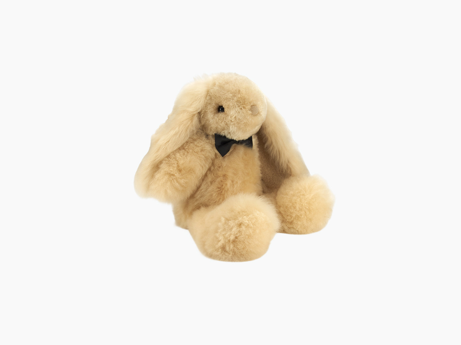 Cream fluffy rabbit with long ears resting on its sides and a black bow tie against a white background.
