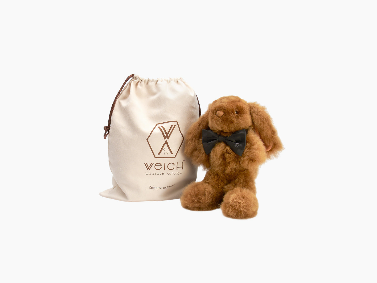 Brown Milo rabbit plush handcrafted from alpaca fiber with a black bow tie beside a beige WEICH drawstring bag.