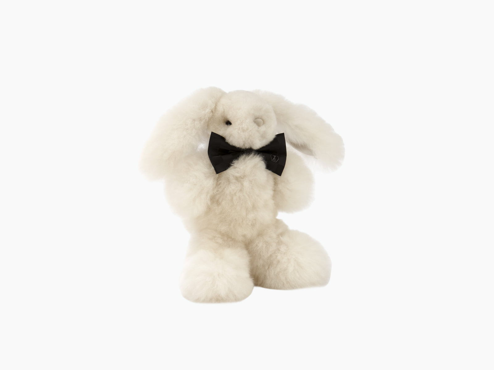 Cream plush rabbit with long ears and a black bow tie seated against a white background.