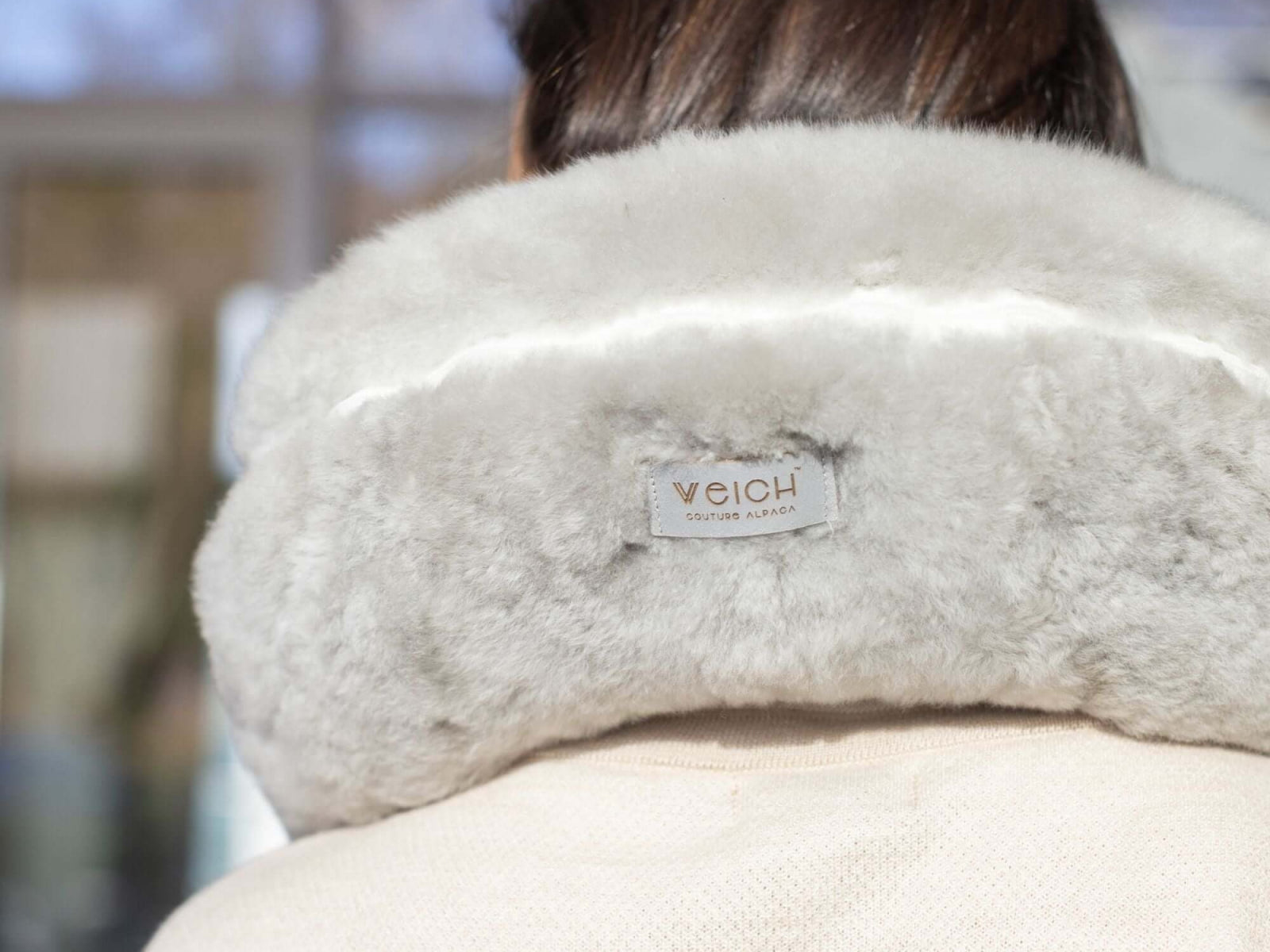 Light gray fluffy alpaca fiber travel pillow with a WEICH label.