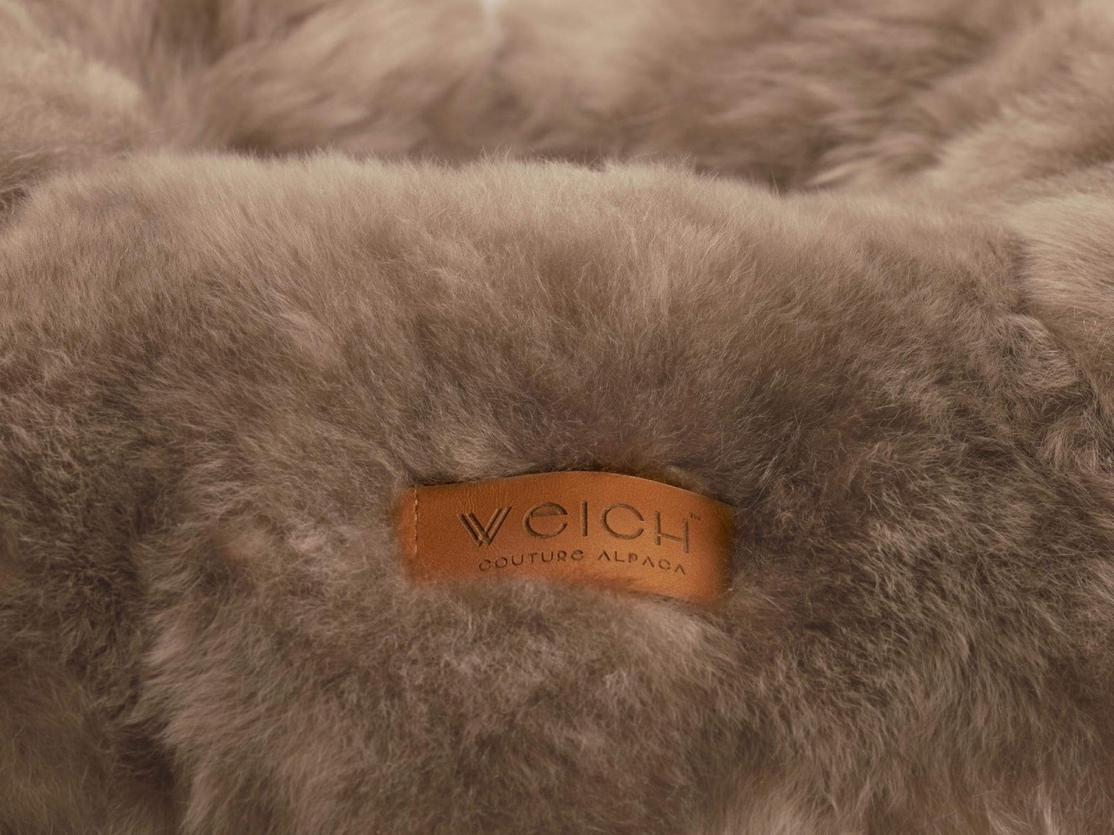 Close up of fluffy taupe fur and a tan leather tag that reads Weich Couture Alpaca.