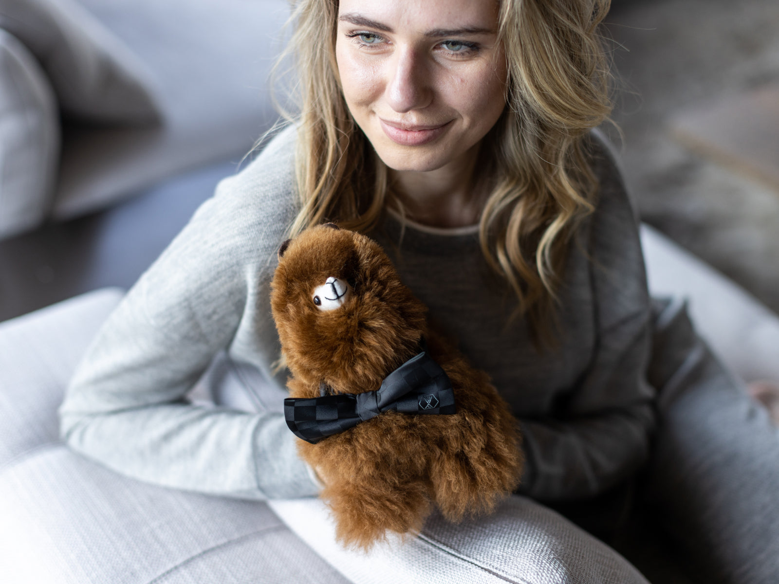 Brown fluffy Alpaca Paco plush with a black bow tie held by a smiling woman