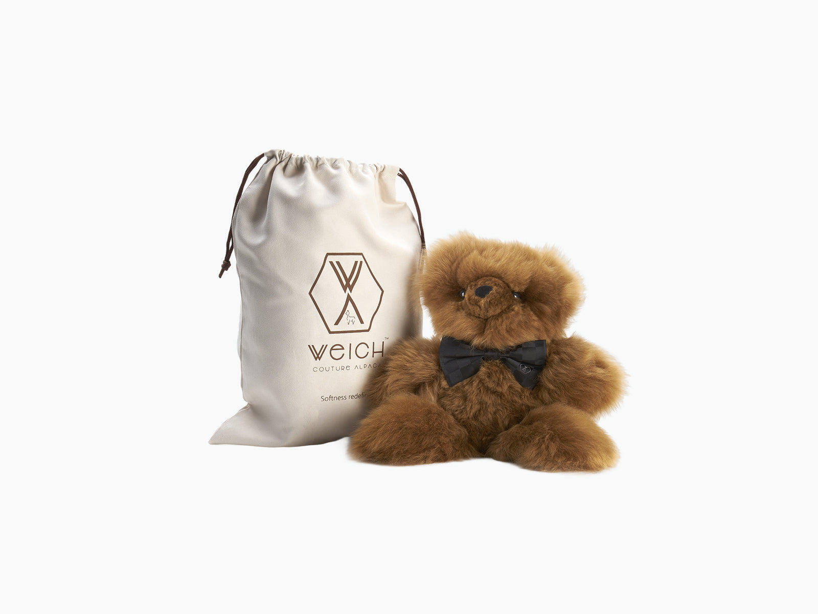 Brown Pelu teddy bear wearing a black silk bow tie beside a WEICH cloth bag